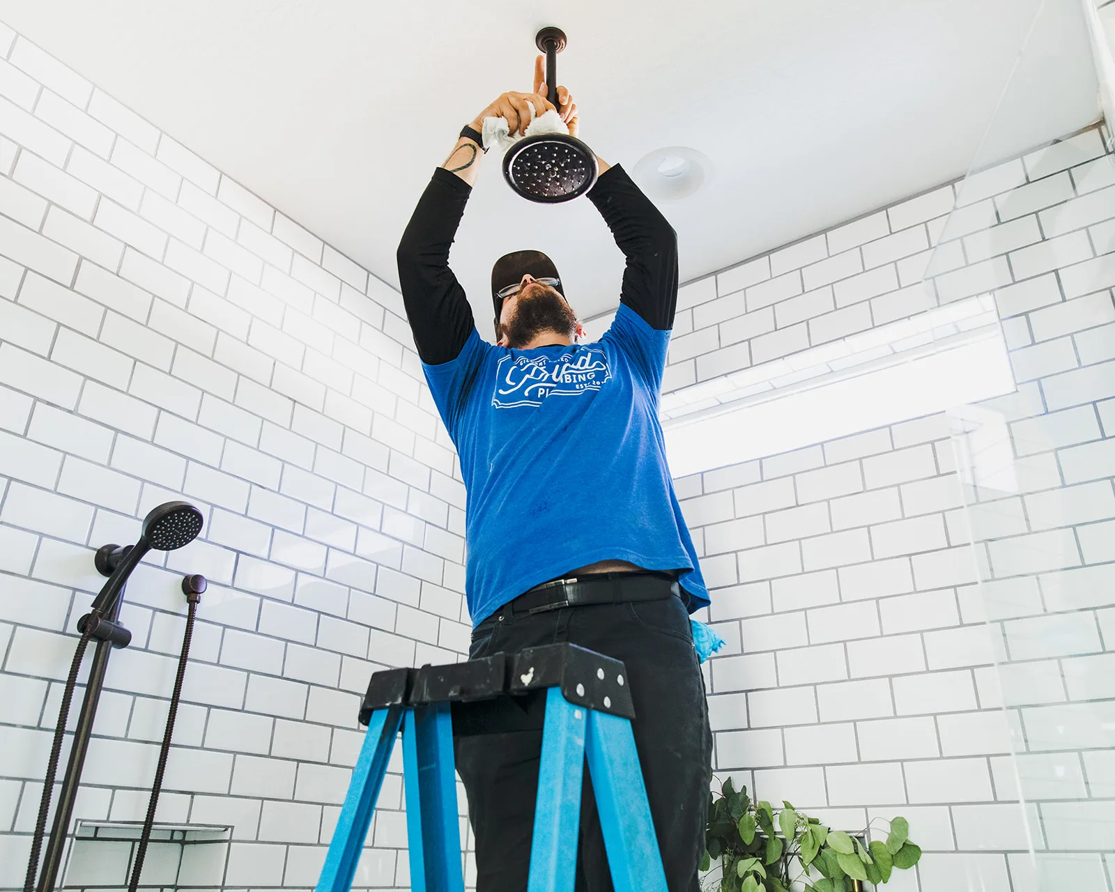Phend Plumbing technician installing a wall-mounted bathroom fixture in a tiled commercial restroom